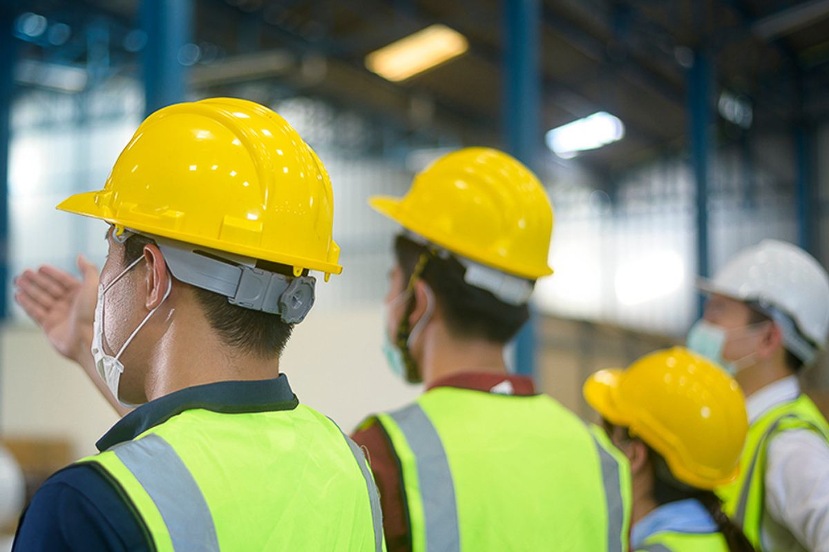 Workers wearing helmets and safety vests discussing on the factory floor