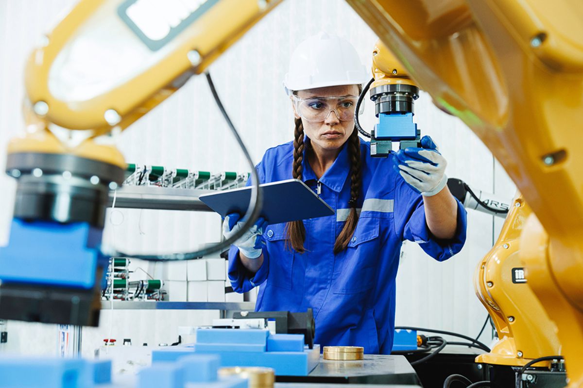 Female worker wearing a helmet collaborating with a robotic arm in a factory