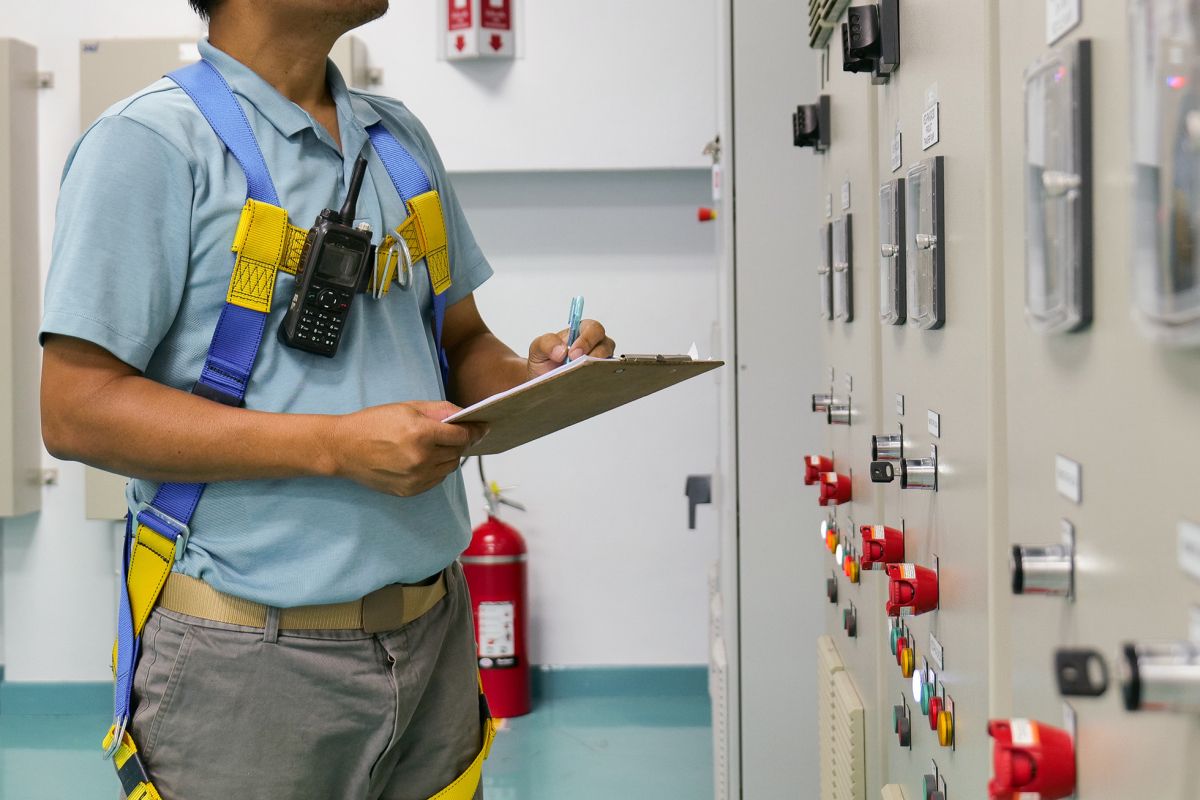 Worker inspecting control panel with a tablet in hand